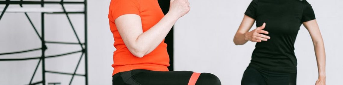 Personal trainer guiding a woman with resistance band exercise in a gym setting.