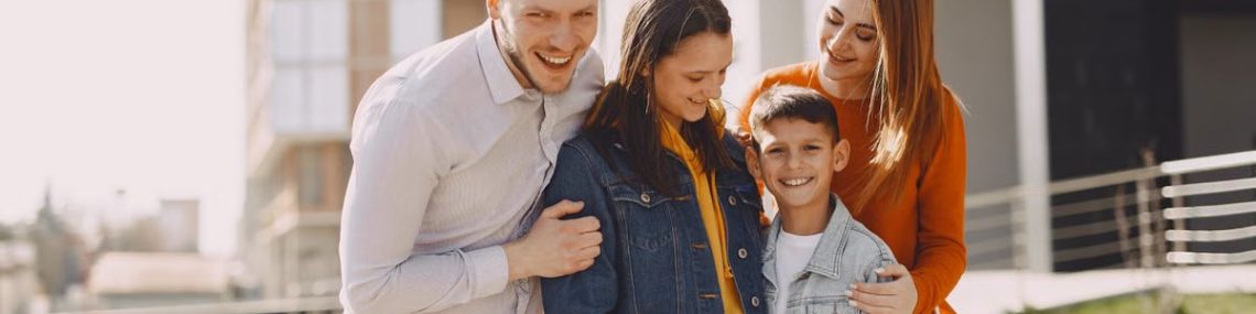 Delighted family in trendy casual wear holding each other and standing near modern building on city street while walking together during weekend